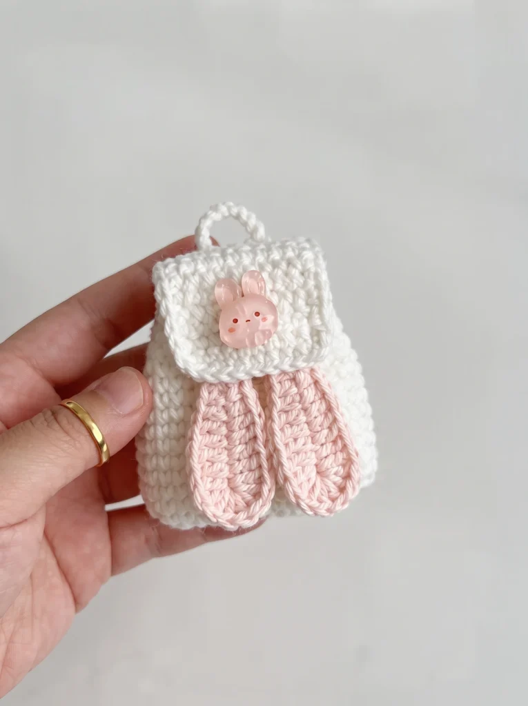 Crochet bunny backpack held in hand for scale, sized for a 20cm doll