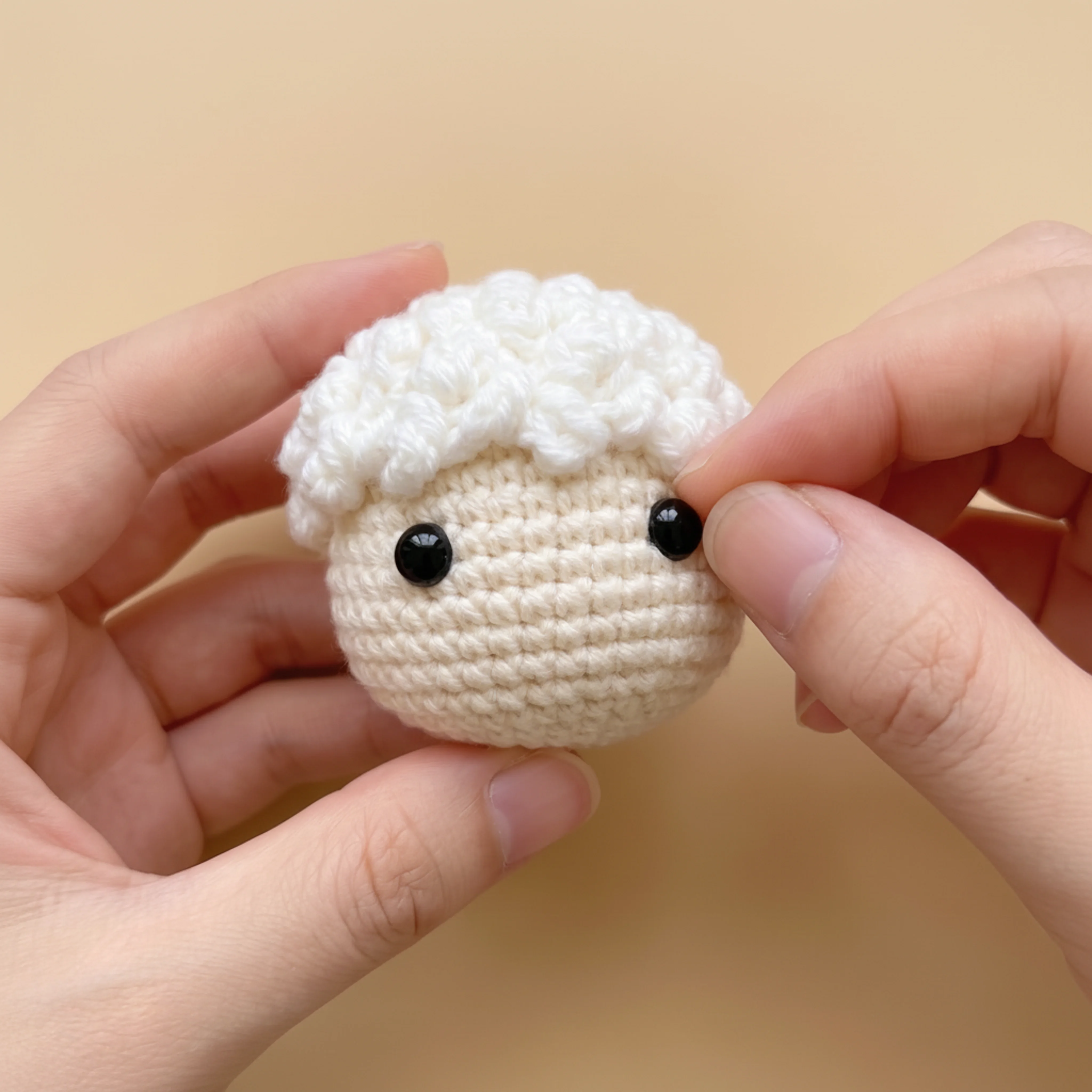 The finished plain head of the crochet lamb keychain, before the wool cap is sewn on