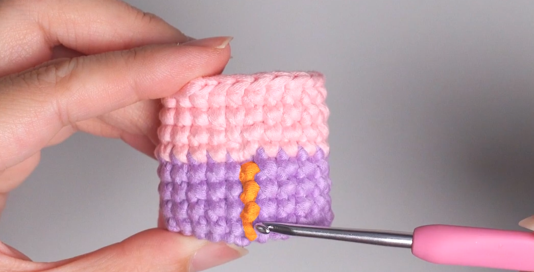 Marking the color change point on a pink and purple crochet cube with contrasting orange yarn